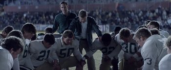 Movie still from “Woodlawn” (2015), directed by Jon Erwin – A group of football players kneeling on a field; Wide shot, High angle