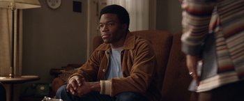 Movie still from “Woodlawn” (2015), directed by Jon Erwin – A man sitting in a chair with his hands crossed; Medium shot, Over the shoulder angle