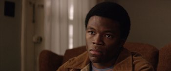 Movie still from “Woodlawn” (2015), directed by Jon Erwin – A man with a brown jacket sitting on a couch; Close Up shot, High angle
