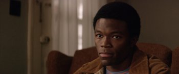 Movie still from “Woodlawn” (2015), directed by Jon Erwin – A man sitting on a couch in a living room; Close Up shot, Over the shoulder angle