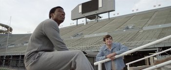 Movie still from “Woodlawn” (2015), directed by Jon Erwin – Two young men sitting in front of bleachers at a football game; Medium shot, Low angle