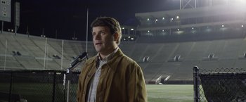 Movie still from “Woodlawn” (2015), directed by Jon Erwin – A man standing in front of a microphone on a football field at night; Medium shot, Low angle