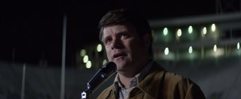 Movie still from “Woodlawn” (2015), directed by Jon Erwin – A man is speaking into a microphone in front of a crowd; Close Up shot, Over the shoulder angle