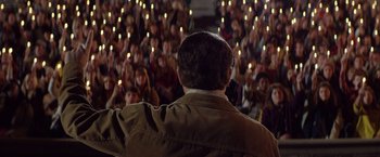 Movie still from “Woodlawn” (2015), directed by Jon Erwin – A crowd of people are gathered in front of a man with his back to the camera; Medium shot, High angle
