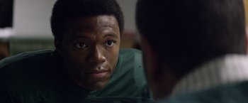 Movie still from “Woodlawn” (2015), directed by Jon Erwin – A young man looking into a mirror while wearing a green shirt; Close Up shot, Over the shoulder angle