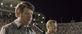 Movie still from “Woodlawn” (2015), directed by Jon Erwin – Two men standing next to each other in front of an audience; Close Up shot, Over the shoulder angle