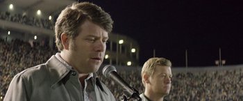 Movie still from “Woodlawn” (2015), directed by Jon Erwin – Two men standing next to each other in front of an audience; Close Up shot, Over the shoulder angle