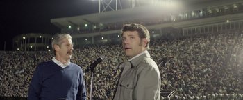 Movie still from “Woodlawn” (2015), directed by Jon Erwin – A man standing in front of a microphone in front of a crowd; Medium shot, Low angle