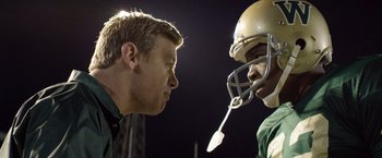 Movie still from “Woodlawn” (2015), directed by Jon Erwin – A man and a football player face each other; Close Up shot, Over the shoulder angle