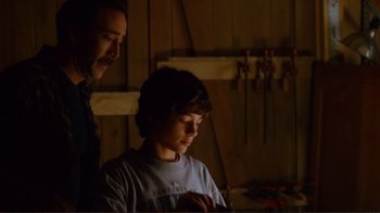Movie still from “World Trade Center” (2006), directed by Oliver Stone – A man standing next to a young boy in a workshop; Medium shot, Over the shoulder angle