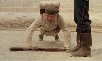 Movie still from “Woyzeck” (1979), directed by Werner Herzog – An old man in a military uniform doing push - ups on the ground; Wide shot, High angle
