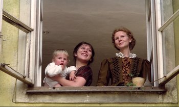 Movie still from “Woyzeck” (1979), directed by Werner Herzog – Two women and a baby looking out of a window; Medium shot, Low angle