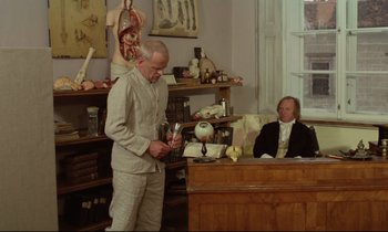 Movie still from “Woyzeck” (1979), directed by Werner Herzog – A man standing next to a desk in a room; Wide shot, Over the shoulder angle