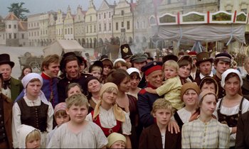 Movie still from “Woyzeck” (1979), directed by Werner Herzog – A group of people in costumes in front of buildings; Wide shot, High angle