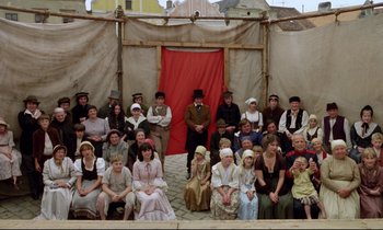 Movie still from “Woyzeck” (1979), directed by Werner Herzog – A group of people sitting in front of a red curtain; Wide shot, High angle