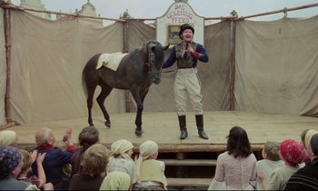 Movie still from “Woyzeck” (1979), directed by Werner Herzog – A man standing next to a horse on a stage; Wide shot, Low angle