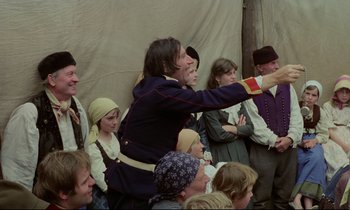 Movie still from “Woyzeck” (1979), directed by Werner Herzog – A group of people gathered around a man in a costume; Medium shot, Over the shoulder angle