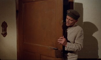 Movie still from “Woyzeck” (1979), directed by Werner Herzog – A man standing in front of an open wooden door; Medium shot, Over the shoulder angle