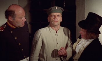 Movie still from “Woyzeck” (1979), directed by Werner Herzog – A man in a military uniform is standing next to two other men; Medium shot, Over the shoulder angle