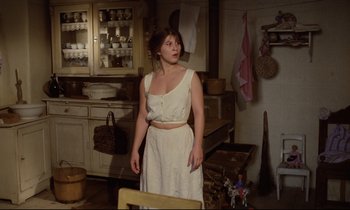 Movie still from “Woyzeck” (1979), directed by Werner Herzog – A woman standing in a kitchen wearing a white dress; Medium shot, High angle