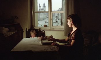 Movie still from “Woyzeck” (1979), directed by Werner Herzog – A woman sitting at a table with a child; Wide shot, High angle