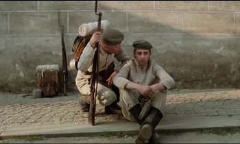 Movie still from “Woyzeck” (1979), directed by Werner Herzog – A man sitting on the ground next to another man holding a rifle; Medium shot, High angle