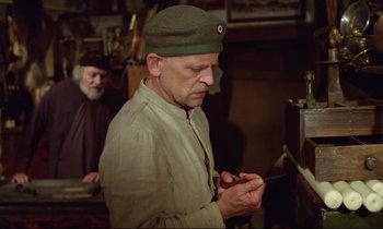Movie still from “Woyzeck” (1979), directed by Werner Herzog – A man in a military uniform looking at a cell phone; Medium shot, Low angle