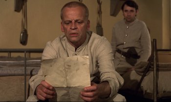 Movie still from “Woyzeck” (1979), directed by Werner Herzog – A man holding a piece of paper while sitting next to another man; Medium shot, Low angle