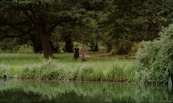 Movie still from “Woyzeck” (1979), directed by Werner Herzog – Two people standing in the grass next to a body of water; Extreme Wide shot, Over the shoulder angle