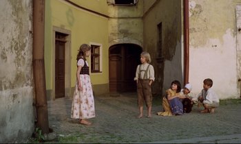 Movie still from “Woyzeck” (1979), directed by Werner Herzog – A group of children sitting on the ground in front of a building; Wide shot, Low angle