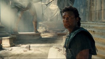 Movie still from “Wrath of the Titans” (2012), directed by Jonathan Liebesman – A man standing next to a statue in a room; Medium shot, Over the shoulder angle
