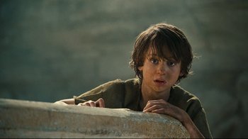Movie still from “Wrath of the Titans” (2012), directed by Jonathan Liebesman – A young boy leaning on a stone wall looking at the camera; Close Up shot, Low angle
