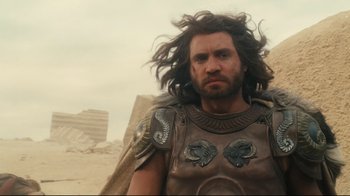 Movie still from “Wrath of the Titans” (2012), directed by Jonathan Liebesman – A man with long brown hair and a beard wearing armor; Medium shot, Over the shoulder angle