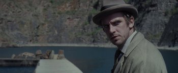 Movie still from “Apostle” (2018), directed by Gareth Evans – A man wearing a hat standing next to a body of water; Close Up shot, Over the shoulder angle