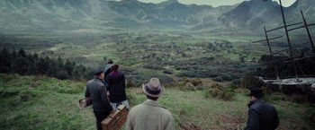 Movie still from “Apostle” (2018), directed by Gareth Evans – A group of people standing on top of a grass covered hill; Wide shot, High angle