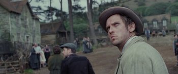 Movie still from “Apostle” (2018), directed by Gareth Evans – A man in a hat and a brown jacket looking into the distance; Close Up shot, Over the shoulder angle
