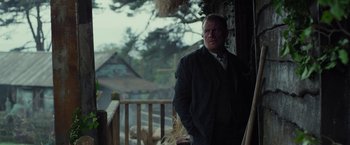 Movie still from “Apostle” (2018), directed by Gareth Evans – A man standing on a porch with his hands in his pockets; Medium shot, Low angle
