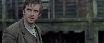 Movie still from “Apostle” (2018), directed by Gareth Evans – A person wearing a suit and tie; Close Up shot, Over the shoulder angle