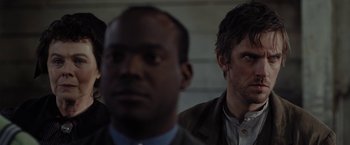 Movie still from “Apostle” (2018), directed by Gareth Evans – Two men in business suits and one man is wearing a suit; Close Up shot, Over the shoulder angle