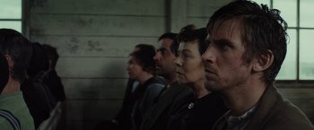 Movie still from “Apostle” (2018), directed by Gareth Evans – A group of people sitting in a row looking at something; Close Up shot, Over the shoulder angle