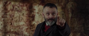 Movie still from “Apostle” (2018), directed by Gareth Evans – A man in a suit and tie pointing at the camera; Close Up shot, Low angle