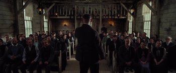 Movie still from “Apostle” (2018), directed by Gareth Evans – A group of people sitting in front of an audience; Wide shot, Low angle