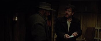 Movie still from “Apostle” (2018), directed by Gareth Evans – Two men are talking in a dimly - lit room; Medium shot, Over the shoulder angle