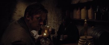 Movie still from “Apostle” (2018), directed by Gareth Evans – A man is drinking a drink at a bar; Medium shot, Over the shoulder angle