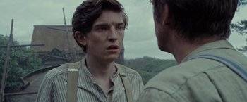 Movie still from “Apostle” (2018), directed by Gareth Evans – A man standing next to another man on a field; Close Up shot, Over the shoulder angle