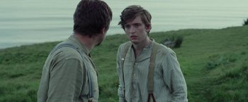 Movie still from “Apostle” (2018), directed by Gareth Evans – Two young men standing next to each other on a field; Medium shot, Over the shoulder angle