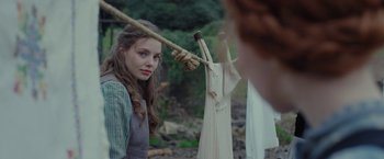 Movie still from “Apostle” (2018), directed by Gareth Evans – A young woman hanging clothes on a rope; Medium shot, Over the shoulder angle