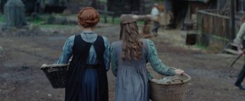 Movie still from “Apostle” (2018), directed by Gareth Evans – Two women are carrying a basket in a field; Medium shot, Over the shoulder angle