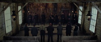 Movie still from “Apostle” (2018), directed by Gareth Evans – A group of men standing in front of each other holding swords; Wide shot, High angle