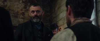 Movie still from “Apostle” (2018), directed by Gareth Evans – A man with a goatee and beard talking to another man; Close Up shot, Over the shoulder angle